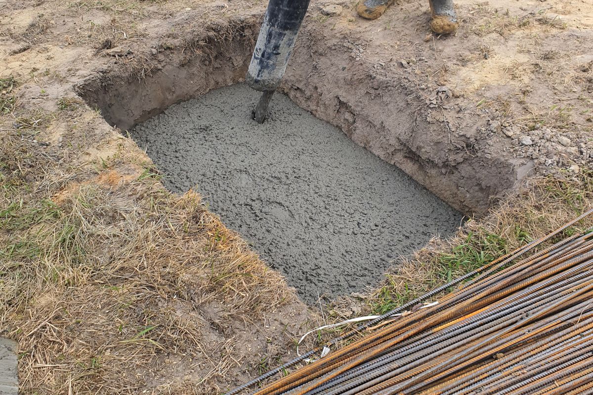 Fresh concrete settling into a formed foundation pit with exposed rebar.